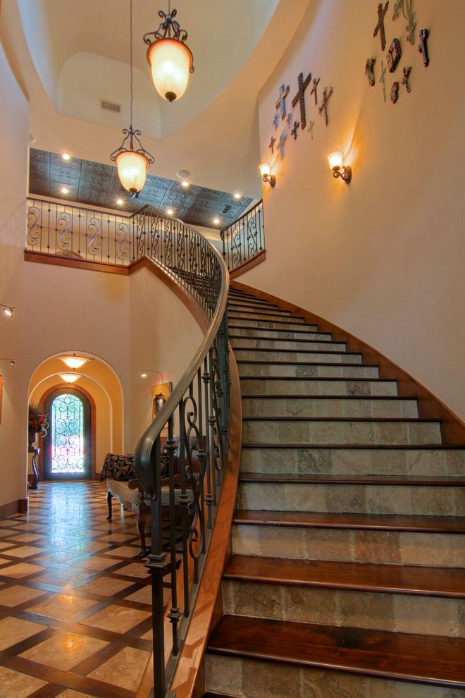 Пример оригинального дизайна: большая изогнутая лестница в средиземноморском стиле с деревянными ступенями, подступенками из сланца и металлическими перилами