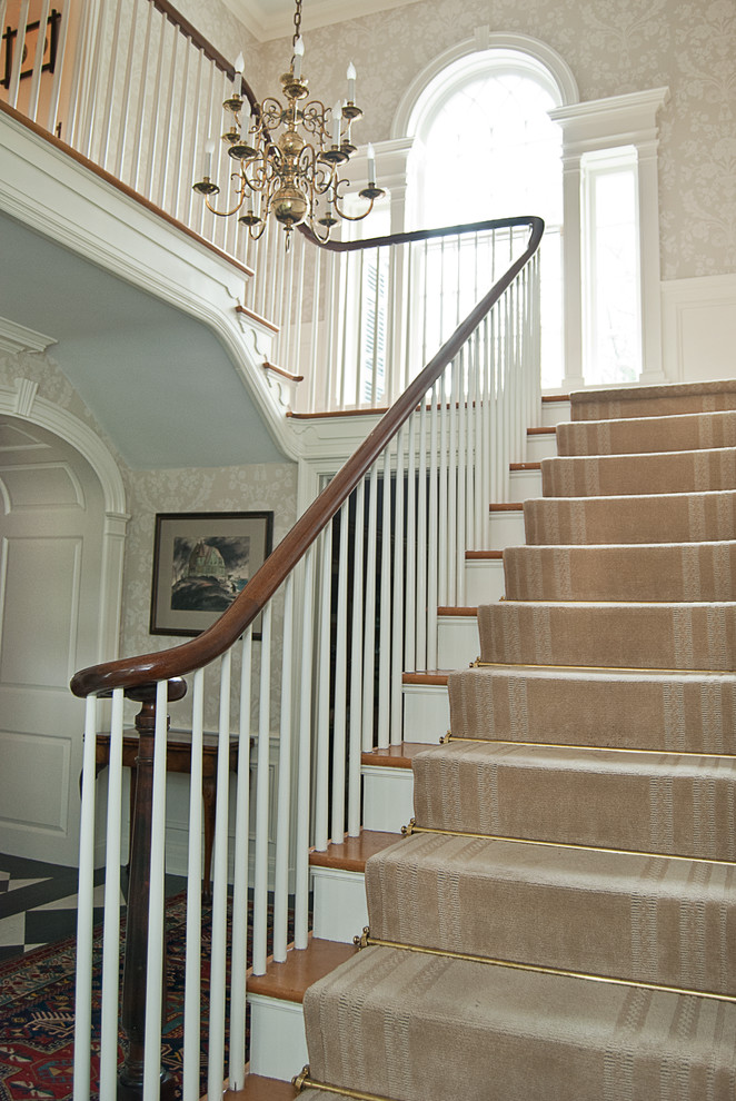 На фото: большая изогнутая лестница в классическом стиле с ступенями с ковровым покрытием, ковровыми подступенками и деревянными перилами с