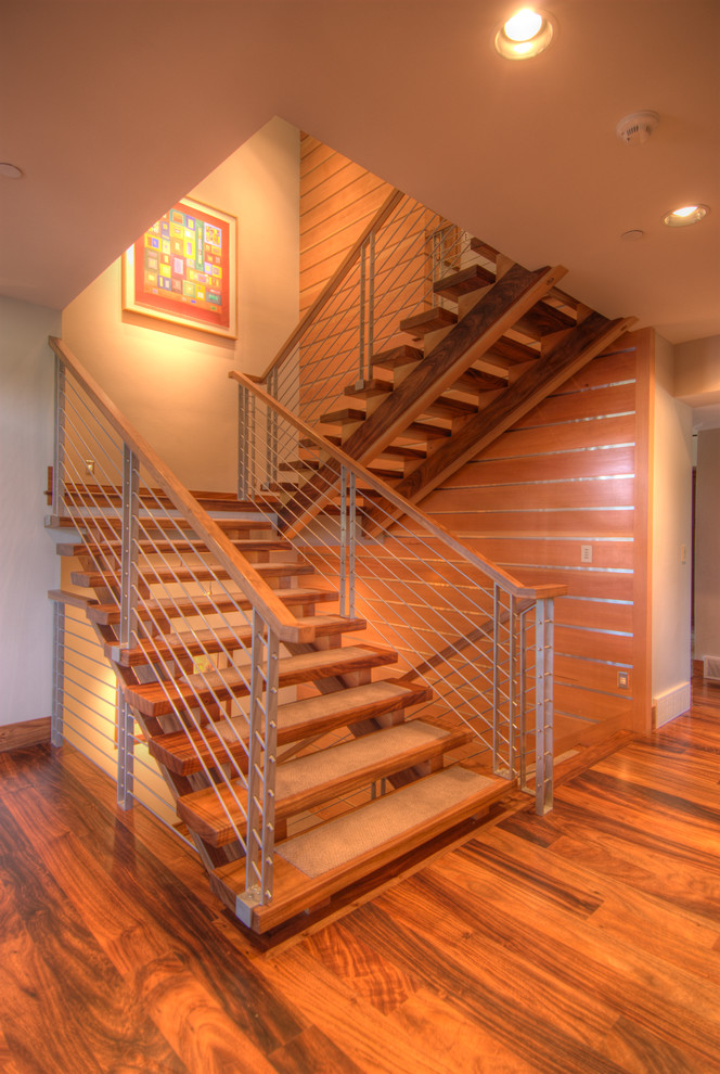 Aménagement d'un grand escalier sans contremarche moderne en U avec des marches en bois, un garde-corps en métal et éclairage.