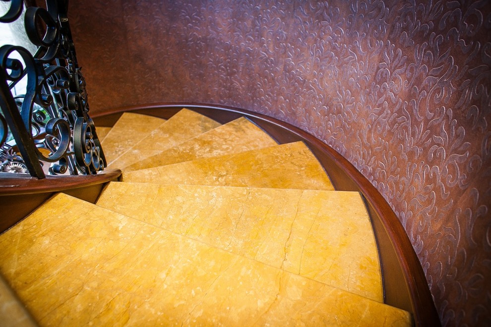 Пример оригинального дизайна: большая изогнутая лестница в средиземноморском стиле с ступенями из известняка, подступенками из известняка и металлическими перилами