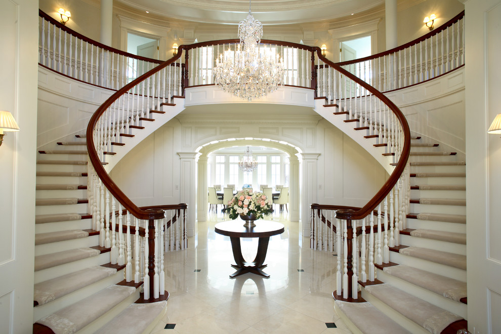 Стильный дизайн: большая изогнутая лестница в классическом стиле с ступенями с ковровым покрытием и крашенными деревянными подступенками - последний тренд