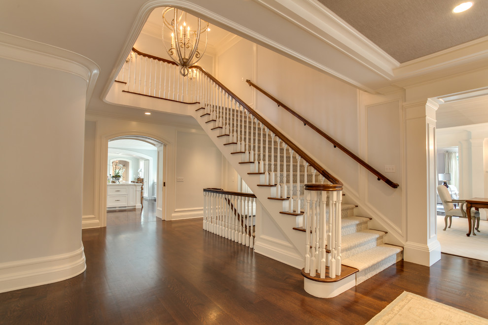 На фото: огромная п-образная лестница в классическом стиле с ступенями с ковровым покрытием, ковровыми подступенками и деревянными перилами с