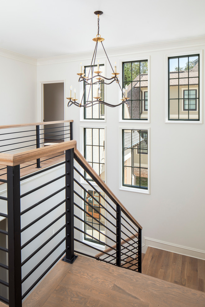 На фото: большая п-образная лестница в стиле неоклассика (современная классика) с деревянными ступенями, крашенными деревянными подступенками и металлическими перилами