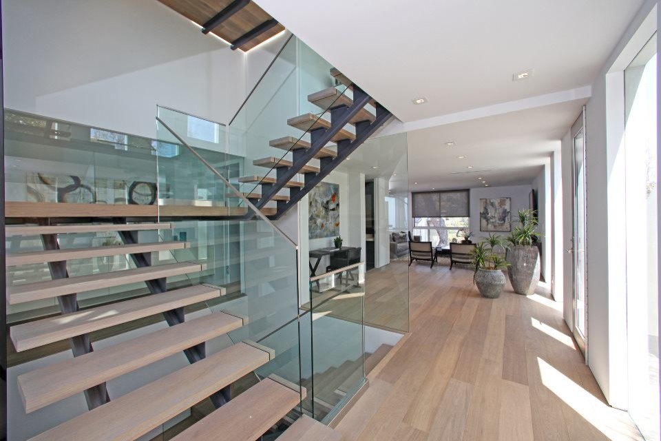 Diseño de escalera suspendida moderna extra grande sin contrahuella con escalones de madera y barandilla de vidrio