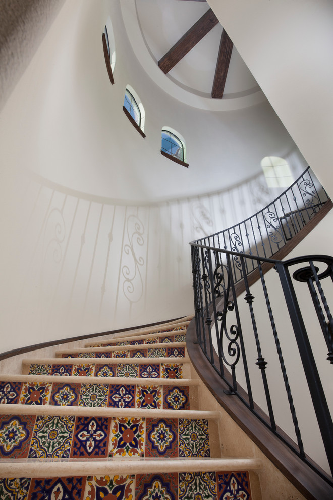 Пример оригинального дизайна: большая изогнутая лестница в средиземноморском стиле с ступенями из плитки и подступенками из плитки