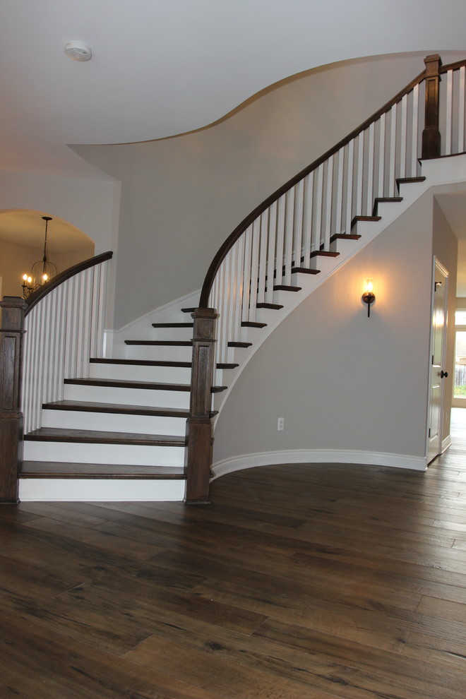 Ejemplo de escalera curva de estilo americano grande con escalones de madera, barandilla de madera y contrahuellas de madera pintada