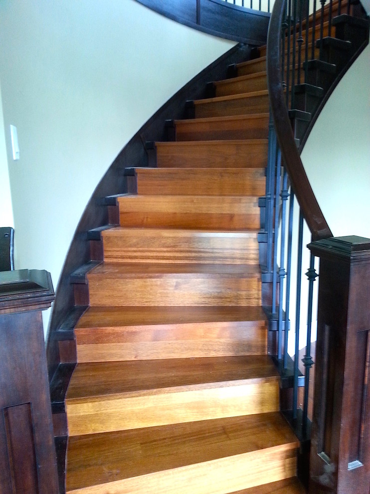 Modelo de escalera curva contemporánea grande con escalones de madera, contrahuellas de madera y barandilla de madera