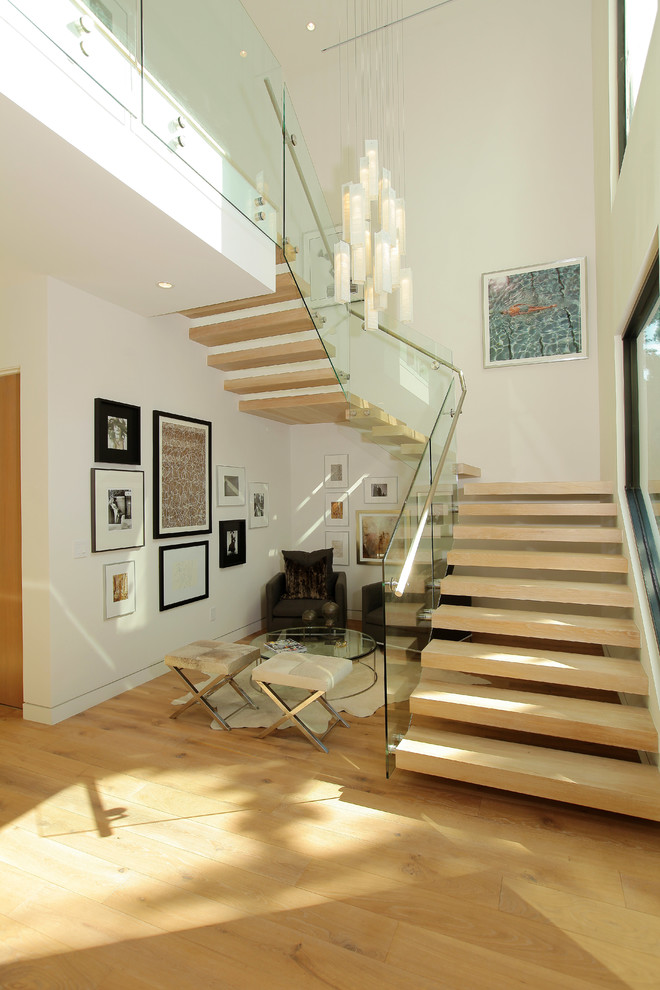 This is an example of a contemporary wood glass railing staircase in Los Angeles with feature lighting.