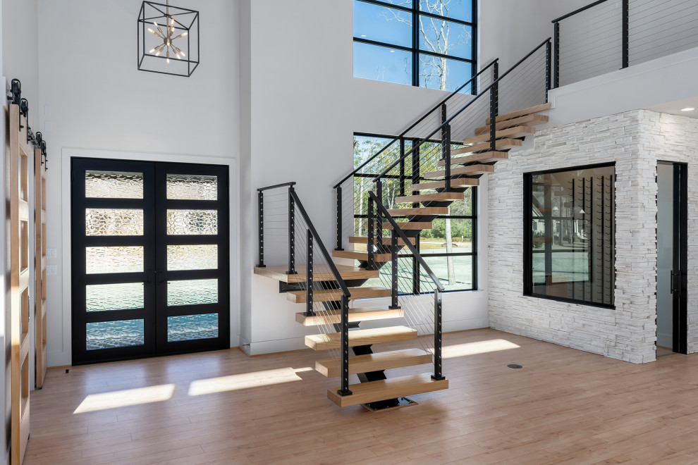 Пример оригинального дизайна: огромная лестница на больцах в стиле модернизм с деревянными ступенями и перилами из тросов без подступенок