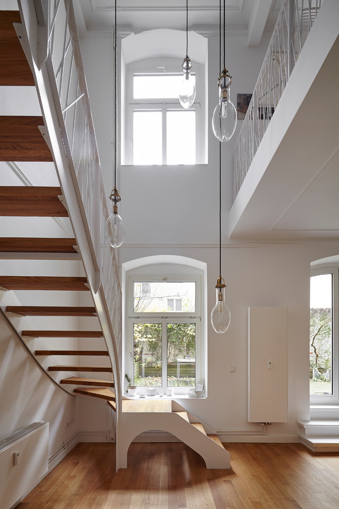 На фото: большая изогнутая лестница в современном стиле с крашенными деревянными ступенями и металлическими перилами без подступенок