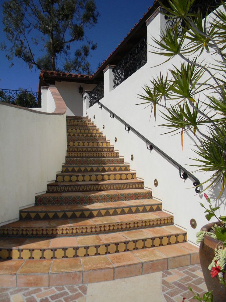 Staircase - mediterranean terra-cotta metal railing staircase idea in San Diego with tile risers