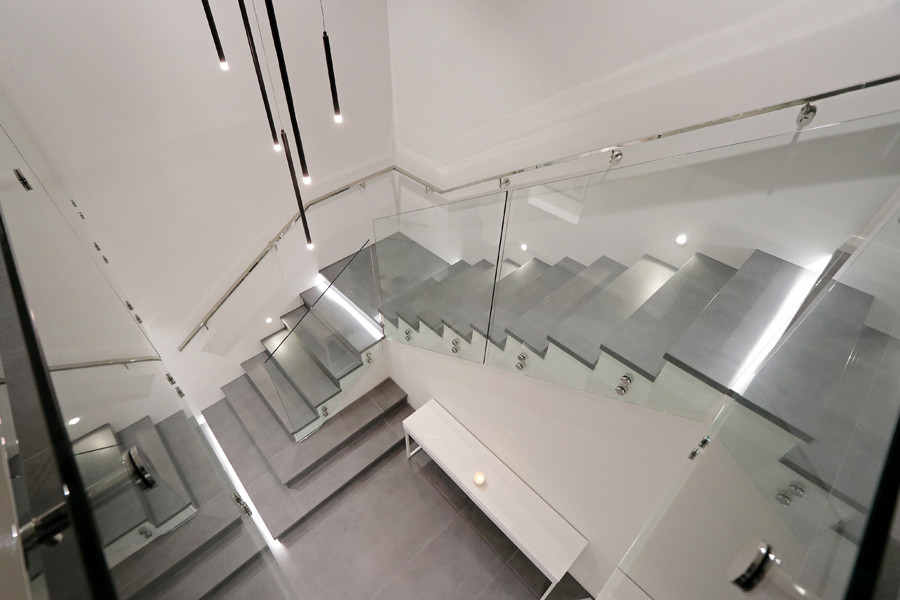 Свежая идея для дизайна: большая угловая лестница в стиле модернизм с ступенями из плитки, подступенками из плитки и стеклянными перилами - отличное фото интерьера