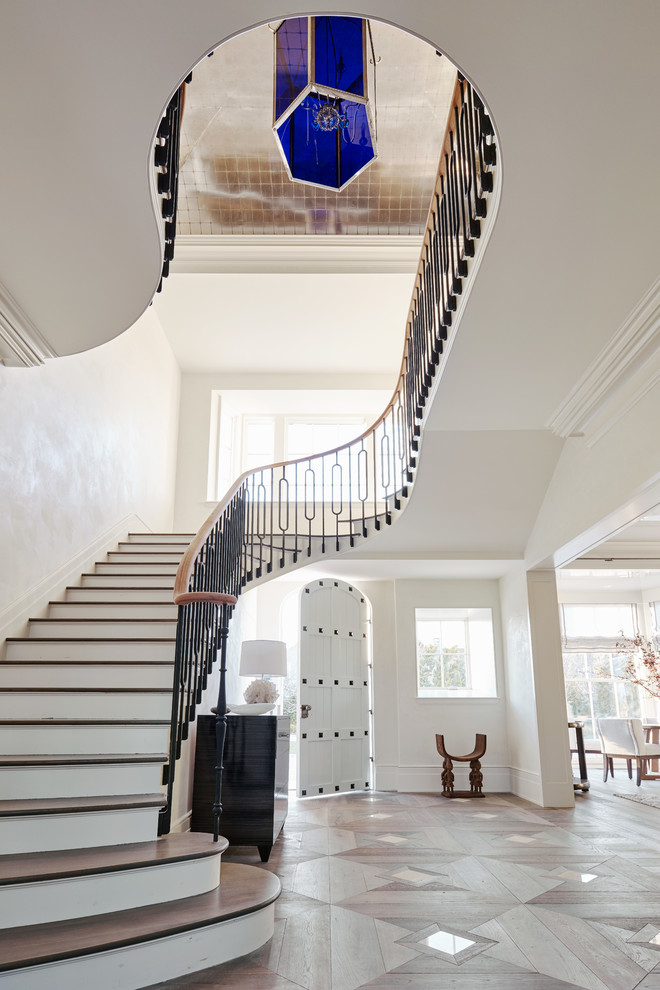 Свежая идея для дизайна: огромная изогнутая лестница в стиле неоклассика (современная классика) с деревянными ступенями и крашенными деревянными подступенками - отличное фото интерьера