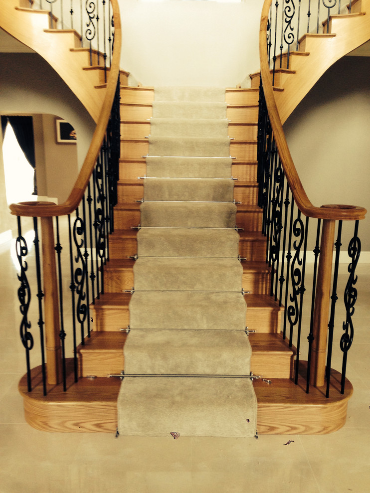 Diseño de escalera curva de estilo de casa de campo grande con escalones de madera, contrahuellas de madera y barandilla de metal