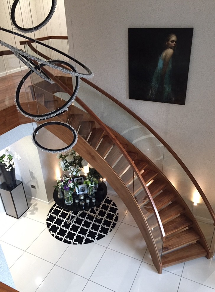 Idée de décoration pour un escalier sans contremarche courbe design de taille moyenne avec des marches en bois et un garde-corps en verre.