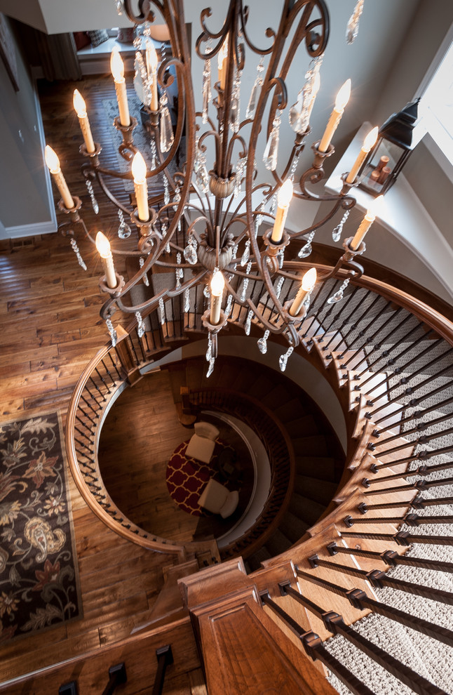 На фото: изогнутая деревянная лестница в стиле рустика с деревянными ступенями и металлическими перилами с
