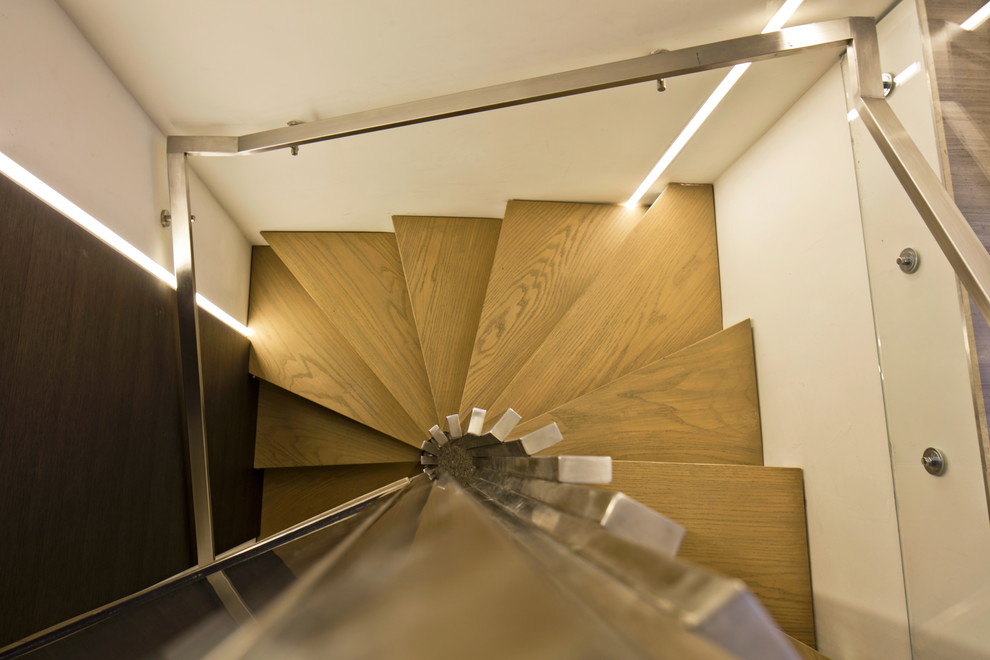 Пример оригинального дизайна: большая винтовая лестница в стиле модернизм с деревянными ступенями и металлическими перилами