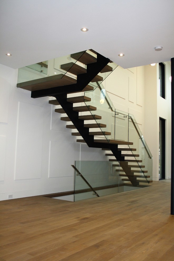Exempel på en stor modern flytande trappa i metall, med sättsteg i metall och räcke i glas