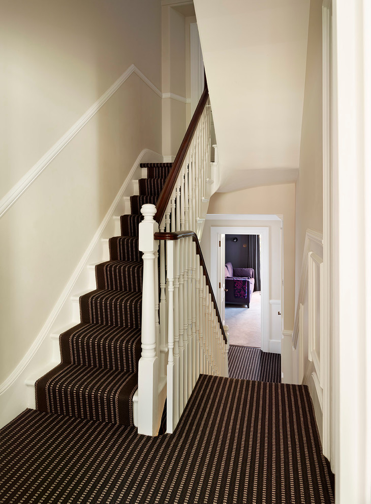На фото: большая угловая лестница в викторианском стиле с ступенями с ковровым покрытием и ковровыми подступенками с