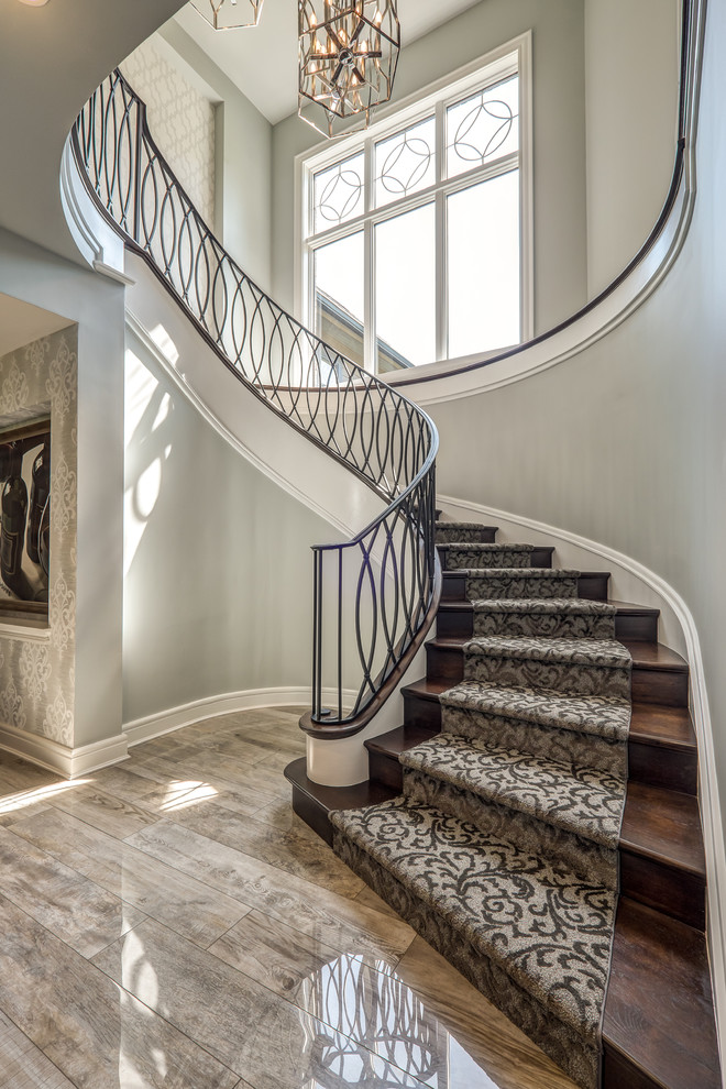 Свежая идея для дизайна: огромная изогнутая лестница в стиле неоклассика (современная классика) с ступенями с ковровым покрытием, ковровыми подступенками и металлическими перилами - отличное фото интерьера