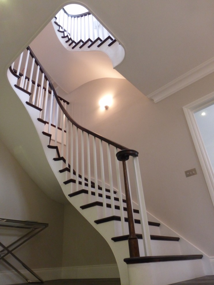 This is an example of an expansive contemporary wood curved staircase in Sussex with painted wood risers.