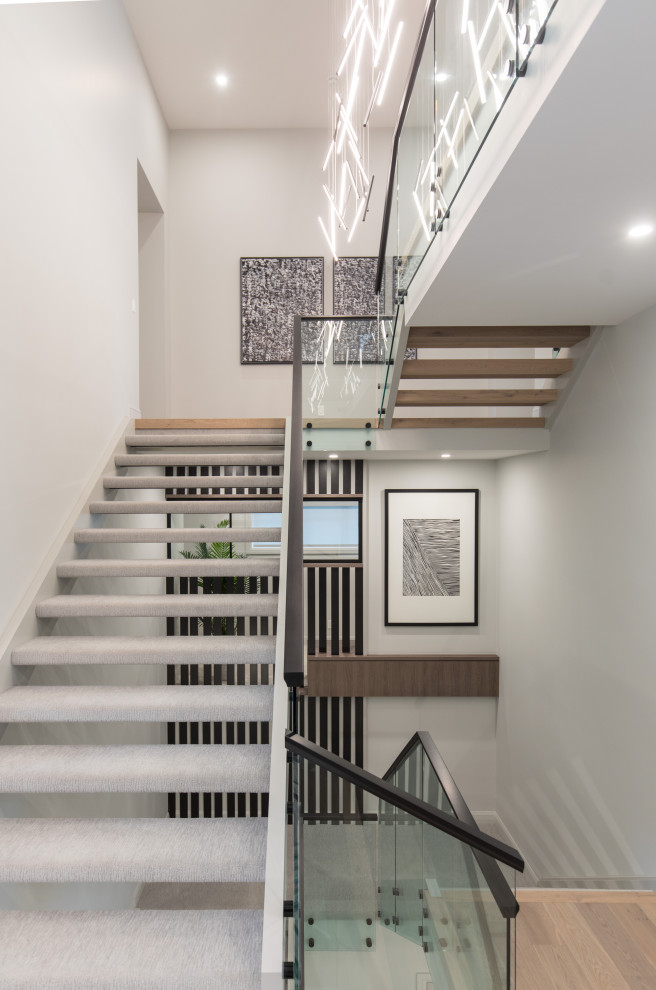 Пример оригинального дизайна: огромная лестница на больцах в современном стиле с ступенями с ковровым покрытием и стеклянными перилами