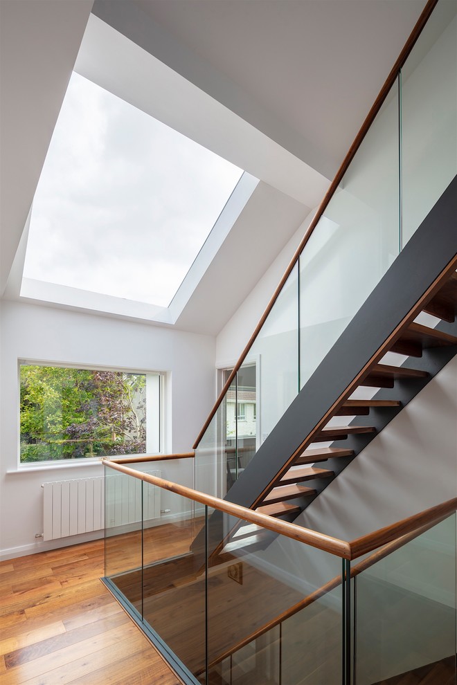 Réalisation d'un grand escalier sans contremarche droit minimaliste avec des marches en bois et un garde-corps en verre.