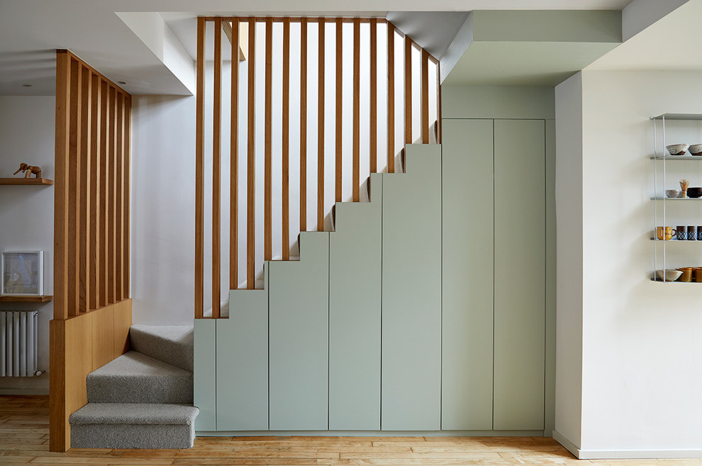 Пример оригинального дизайна: лестница среднего размера в стиле модернизм с ступенями с ковровым покрытием, ковровыми подступенками, деревянными перилами и кладовкой или шкафом под ней