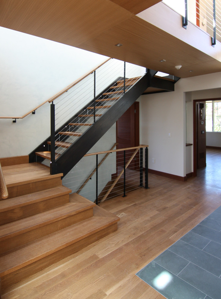 Пример оригинального дизайна: большая п-образная лестница в современном стиле с деревянными ступенями, стеклянными подступенками и перилами из тросов