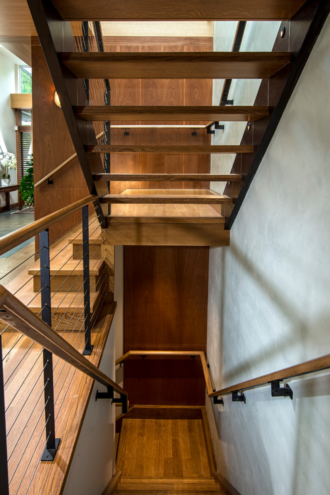 На фото: большая п-образная лестница в современном стиле с деревянными ступенями, стеклянными подступенками и перилами из тросов