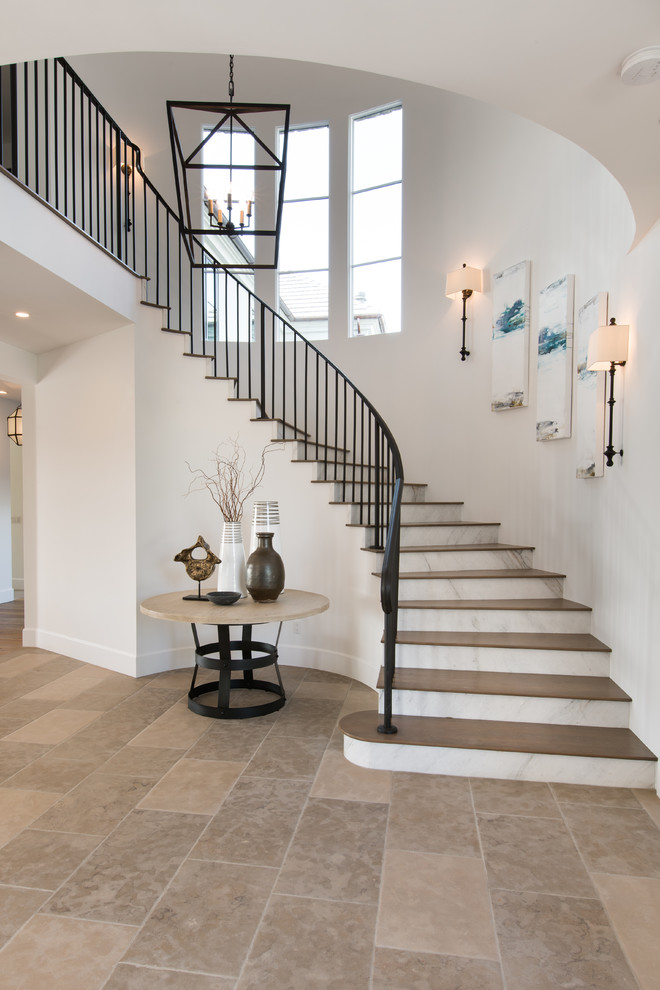 Aménagement d'un grand escalier courbe classique avec des marches en bois, des contremarches en marbre et un garde-corps en métal.