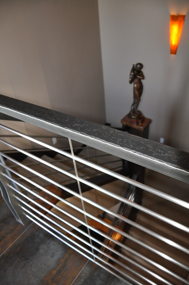 他の地域にあるお手頃価格の中くらいなインダストリアルスタイルのおしゃれな折り返し階段 (木の蹴込み板、金属の手すり) の写真