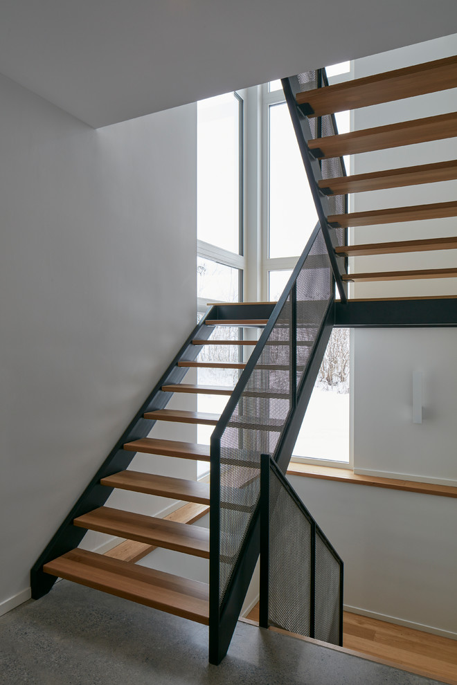 Aménagement d'un grand escalier sans contremarche industriel en U avec des marches en bois et un garde-corps en métal.