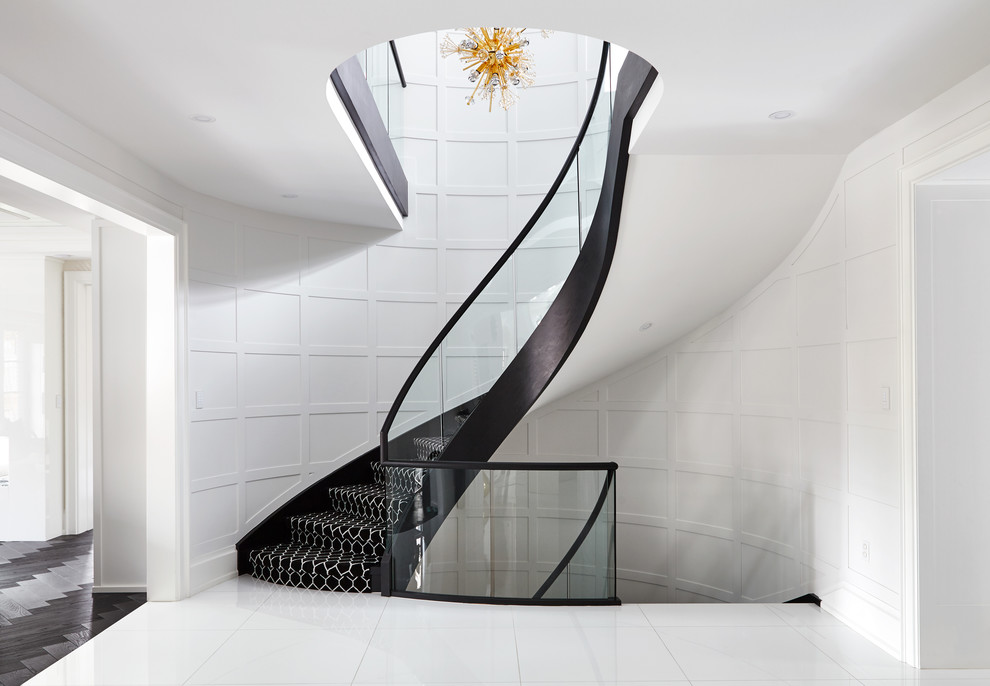 Свежая идея для дизайна: большая изогнутая лестница в стиле неоклассика (современная классика) с ступенями с ковровым покрытием, ковровыми подступенками и стеклянными перилами - отличное фото интерьера
