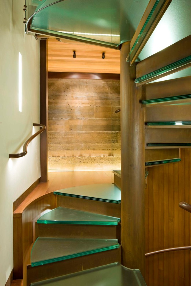 Réalisation d'un grand escalier hélicoïdal minimaliste avec des marches en verre, des contremarches en métal et un garde-corps en bois.