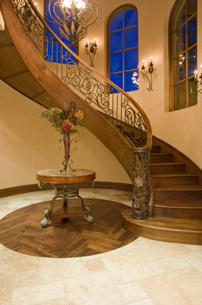 На фото: огромная изогнутая деревянная лестница в средиземноморском стиле с деревянными ступенями и перилами из смешанных материалов с