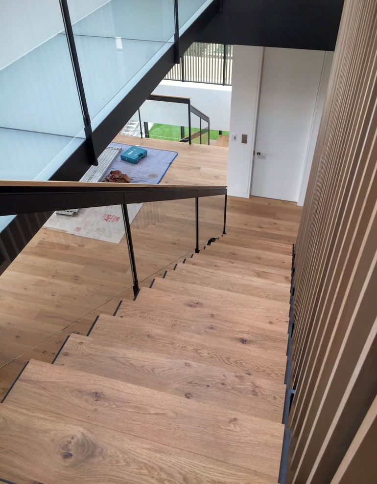 Ejemplo de escalera en L minimalista grande con escalones de madera, contrahuellas de metal y barandilla de vidrio