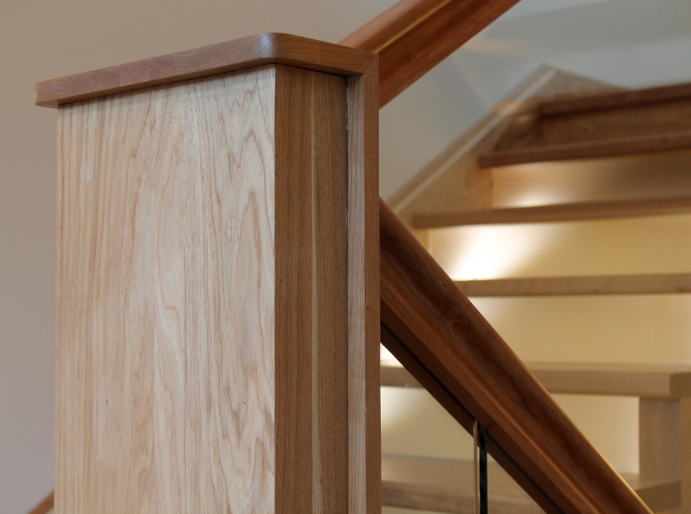 На фото: большая п-образная лестница в современном стиле с крашенными деревянными ступенями, стеклянными подступенками и деревянными перилами с