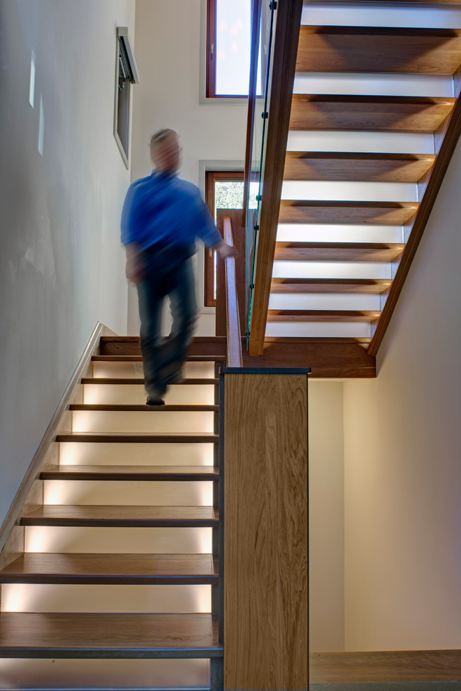 Cette photo montre un grand escalier tendance en U avec des marches en bois peint, un garde-corps en bois et des contremarches en verre.