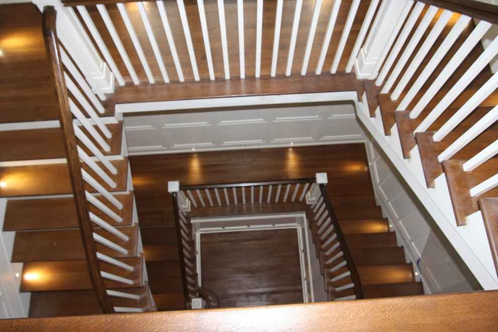 ニューヨークにあるラグジュアリーな巨大なトラディショナルスタイルのおしゃれな折り返し階段 (フローリングの蹴込み板、木材の手すり) の写真