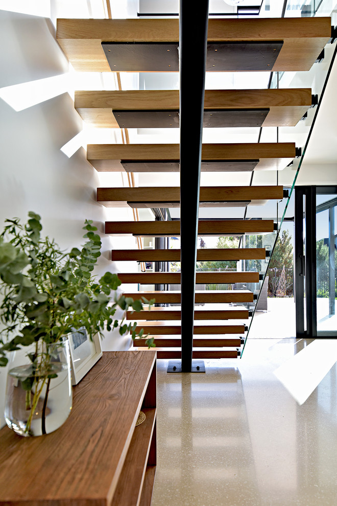 На фото: большая лестница на больцах в стиле модернизм с деревянными ступенями и стеклянными подступенками