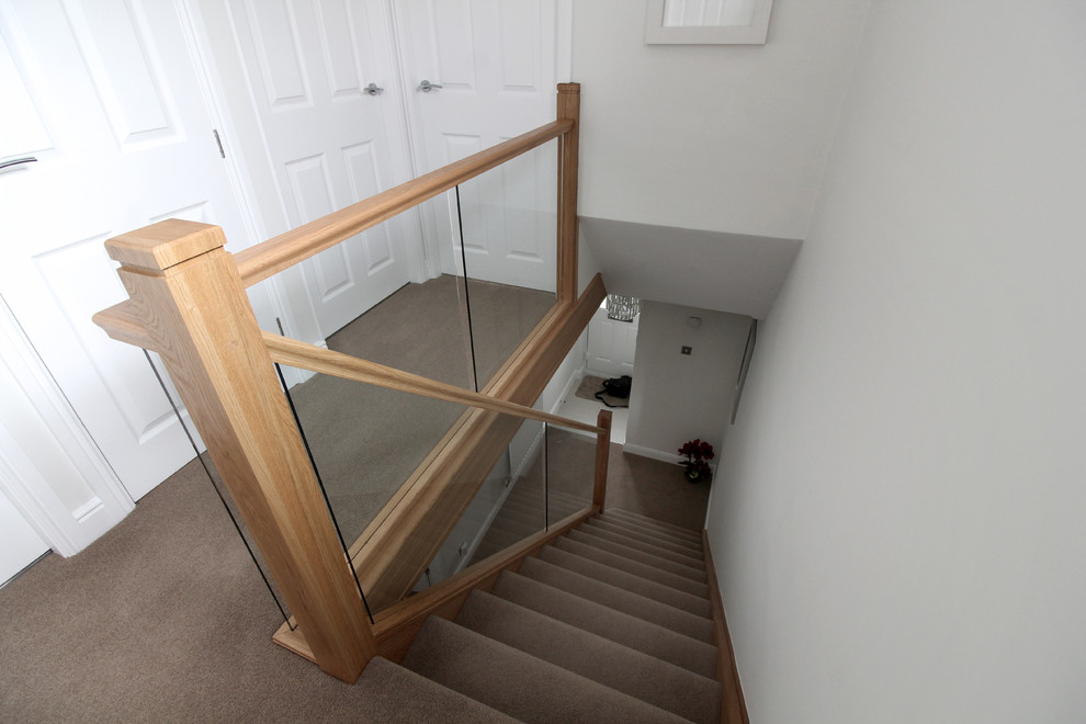 Small modern carpeted straight glass railing staircase in West Midlands with carpeted risers.