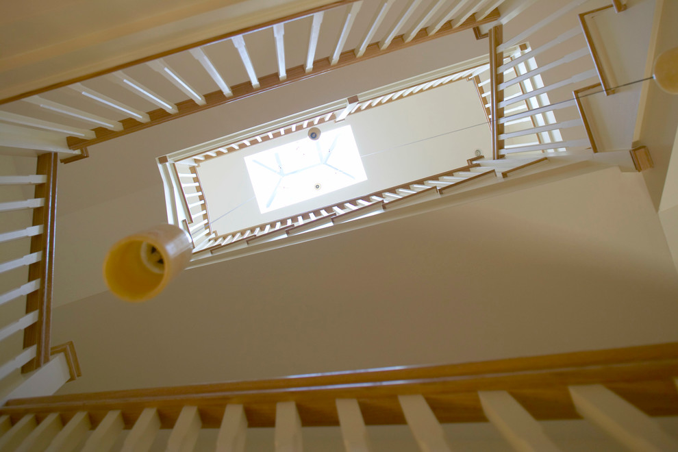 Пример оригинального дизайна: большая лестница в стиле неоклассика (современная классика) с деревянными ступенями, крашенными деревянными подступенками и деревянными перилами