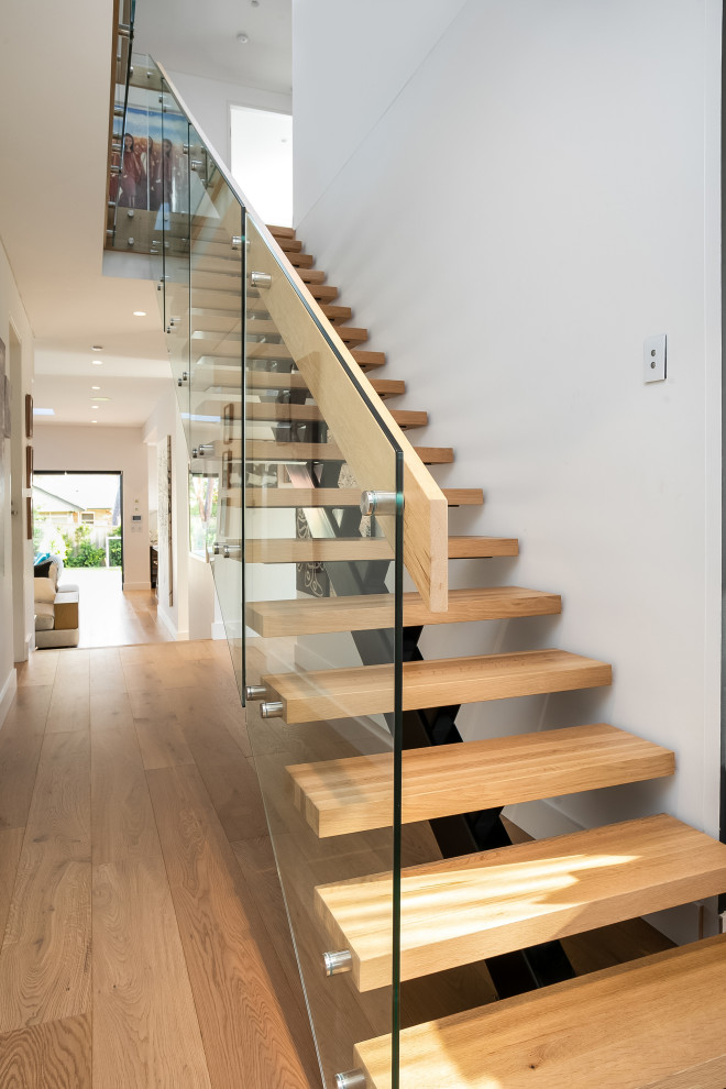 Aménagement d'un grand escalier sans contremarche droit contemporain avec des marches en bois et un garde-corps en verre.