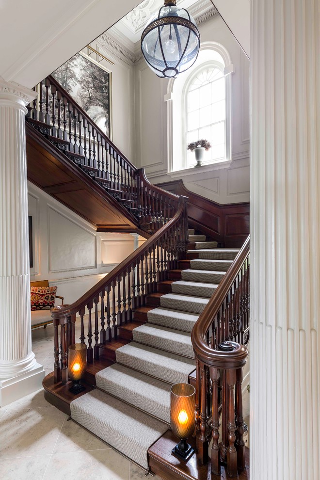 Пример оригинального дизайна: большая изогнутая лестница в классическом стиле с ступенями с ковровым покрытием, ковровыми подступенками и деревянными перилами