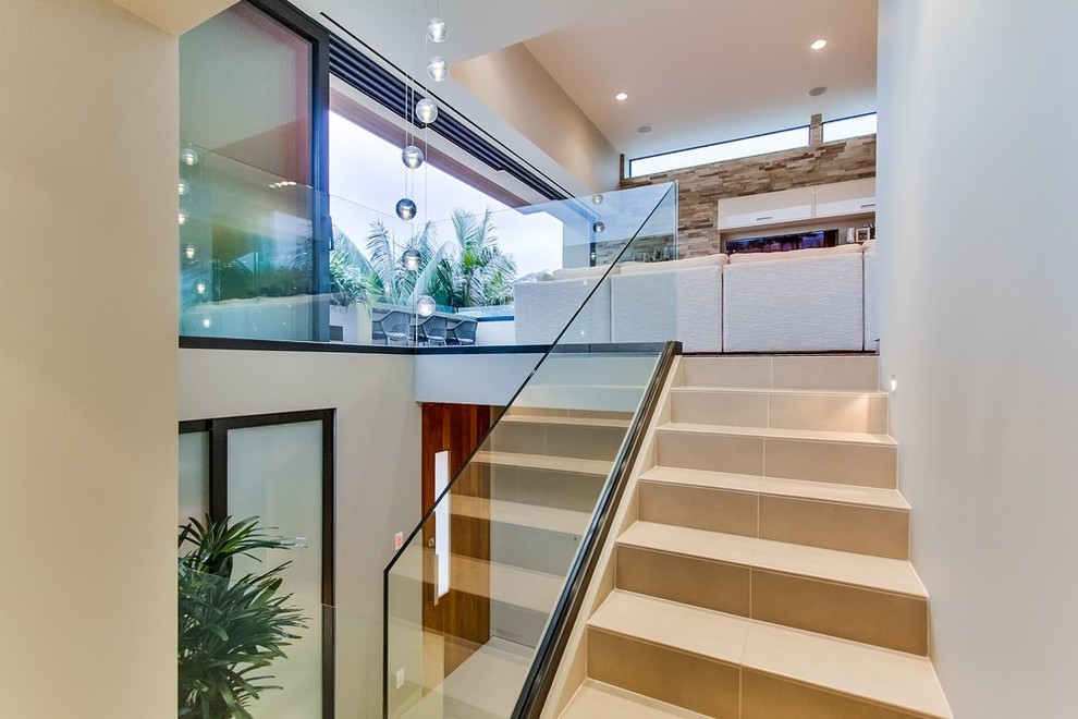 На фото: п-образная лестница среднего размера в современном стиле с ступенями из плитки, подступенками из плитки и стеклянными перилами