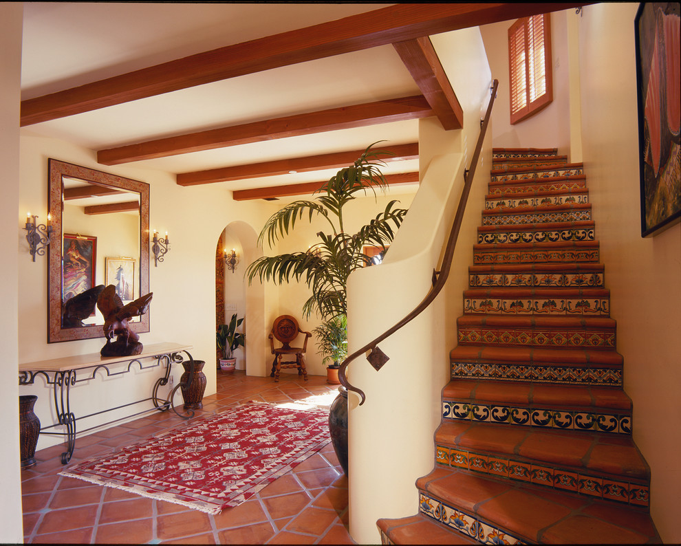 На фото: изогнутая лестница среднего размера в средиземноморском стиле с подступенками из плитки, ступенями из терракотовой плитки и металлическими перилами с