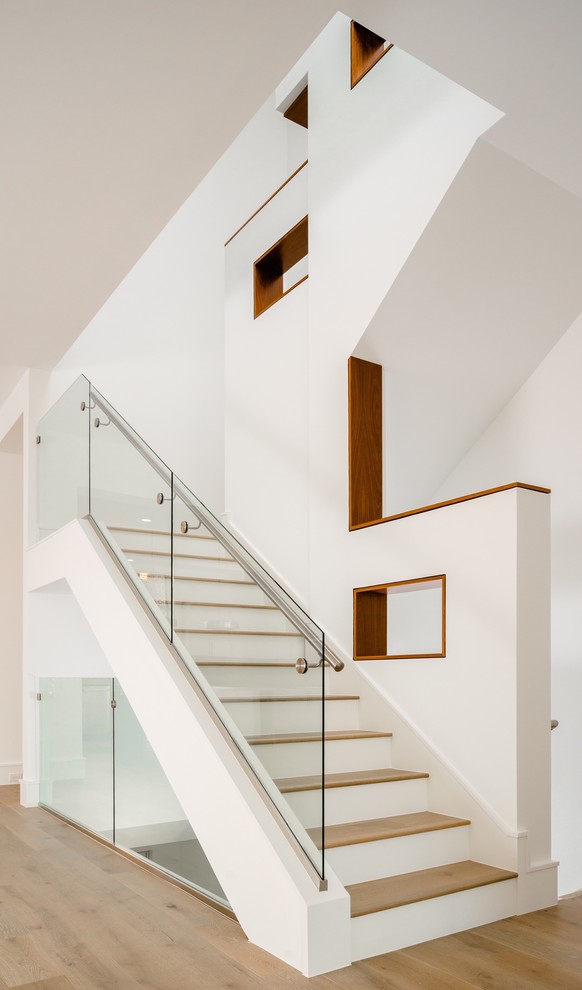 Пример оригинального дизайна: п-образная лестница в современном стиле с деревянными ступенями, крашенными деревянными подступенками и стеклянными перилами