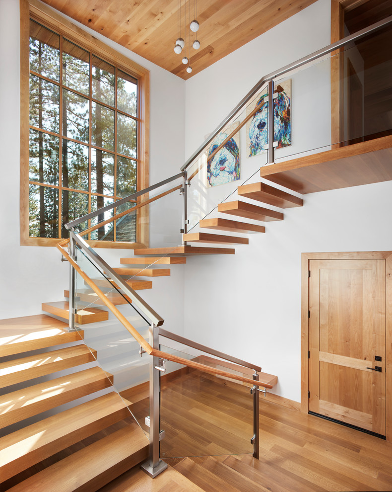 Стильный дизайн: большая лестница на больцах в стиле неоклассика (современная классика) с деревянными ступенями и стеклянными перилами без подступенок - последний тренд
