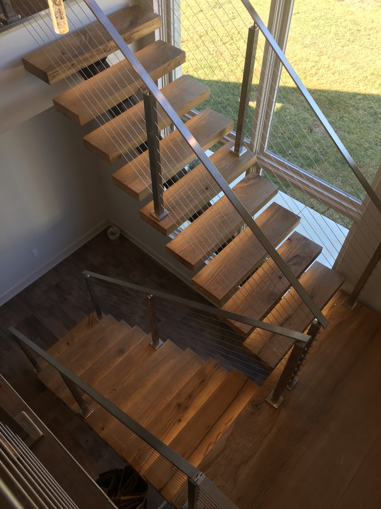 На фото: лестница на больцах, среднего размера в стиле модернизм с деревянными ступенями и перилами из тросов без подступенок